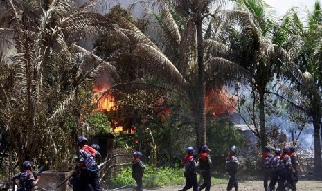 In this photo taken on June 12, 2012, Myanmar policemen walk towards burning buildings in Sittwe, capital of Rakhine state in western Myanmar. Communal violence is grinding on in western Myanmar six weeks after the government declared a state of emergency 