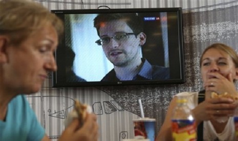 In this Wednesday, June 26, 2013 file photo transit passengers eat at a cafe with   a TV screen with a news program showing a report on Edward Snowden, in the   background, at Sheremetyevo airport in Moscow, Russia.