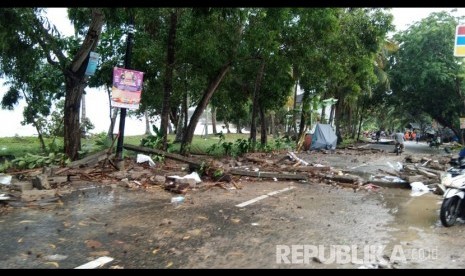 Jalan Raya Anyer, Ahad (23/12), sulit dilalui kendaraan roda empat karena terhambat puing. Petugas dan warga tampak berupaya membersihkan puing dari jalanan.