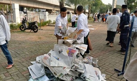 Jamaah di Masjid Al Azhar mengumpulkan koran yang dijadikan alas Shalat Idul Fitri menjadi satu tumpukan agar tidak berserakan di sekitar masjid, Jumat (15/6).