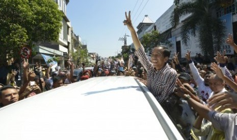 Joko Widodo (kanan) mengacungkan salam dua jari kepada warga ketika berkunjung ke kawasan Pasar Kota, Gresik, Jawa Timur, Ahad (29/6). 