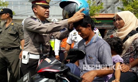 Kanit Regident Polres Indramayu, Iptu Tenda, memasangkan helm kepada seorang pengguna sepeda motor yang diketahui tidak mengenakan helm saat berkendara, Senin (6/3).