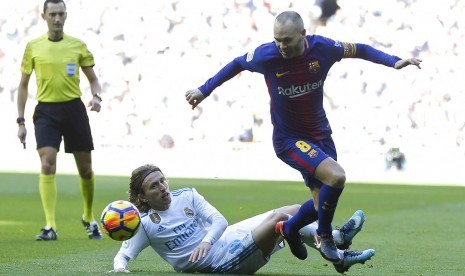 Kapten Barcelona, Andres Iniesta (kanan) berusaha dijegal oleh gelandang Real Madrid, Luka Modric pada laga el Clasico di Santiago Bernabeu, Sabtu (23/12). Barca menang 3-0 pada laga ini.