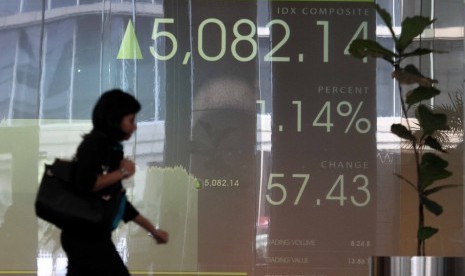 Karyawan melintas di depan layar Indeks Harga Saham Gabungan (IHSG) di Bursa Efek Indonesia, Jakarta, Kamis (10/7). 