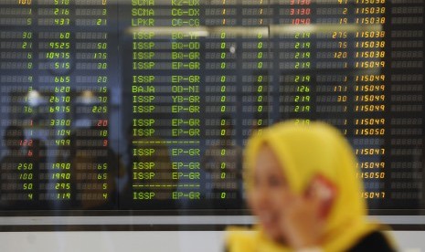 Karyawan melintas di depan layar pergerakan Indeks Harga Saham Gabungan (IHSG) di Mandiri Sekuritas, Jakarta, Selasa (12/4).  (Antara/Sigid Kurniawan)