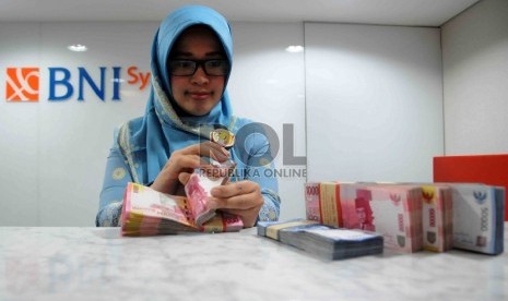 Karyawan menghitung uang di Banking Hall Bank BNI Syariah, Jakarta.