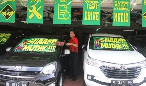 Karyawan pemasaran membersihkan mobil bekas yang dijual di ruang pamer.