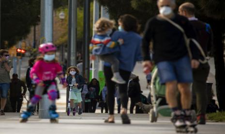 Keluarga bersama anank-anak mereka berjalan di sepanjang sisi Barcelona, Spanyol, (26/4). Mulai kemarin anak-anak di bawah 14 tahun boleh keluar rumah dengan orang tuanya selama satu jam dan dengan jarak maksimal 1 km dari rumah. 