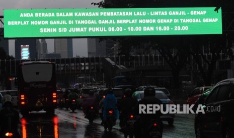 Kendaraan melintas di dekat papan informasi kebijakan sistem pembatasan kendaraan bermotor berdasarkan nomor pelat ganjil-genap di Sudirman, Jakarta.