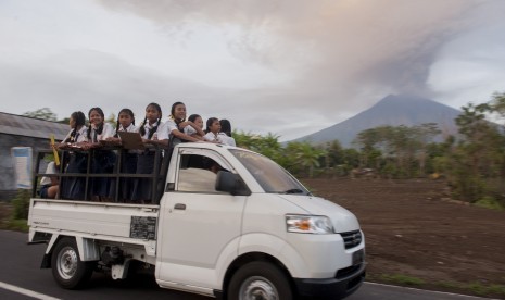 Kendaraan mengangkut siswa dengan latar belakang asap dan abu vulkanik menyembur dari kawah Gunung Agung di Desa Datah, Karangasem, Bali, Senin (27/11). 