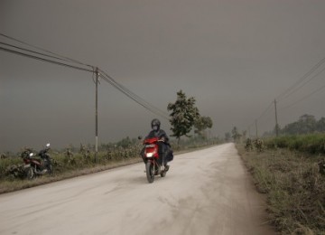 Kendaraan melintas di jalan raya Muntilan-Borobudur, dengan latar belakang langit gelap tertutup material vulkanik Gunung Merapi di Desa Mendut, Mungkid, Magelang, Jateng