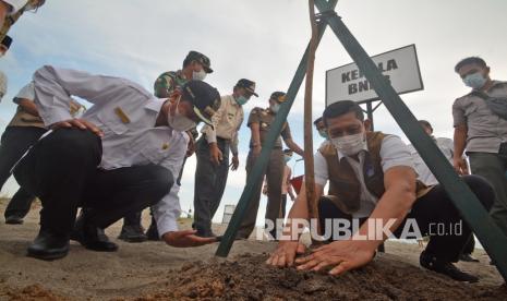 Kepala BNPB Doni Monardo (kanan), ditemani Wali Kota Pariaman, Genius Umar (kiri) menambahkan pupuk pada bibit pohon pinago, di Pantai Taluak Pariaman, Sumatera Barat, Rabu (14/4/2021). Doni Monardo menyatakan mitigasi berbasis alam dengan penanaman pohon pelindung pantai merupakan salah satu solusi terbaik di samping kesiapsiagaan masyarakat, apalagi di Sumbar yang memiliki risiko bencana tinggi. 