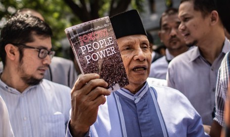 Ketua Dewan Kehormatan Partai Amanat Nasional (PAN) Amien Rais (tengah) menunjukkan buku berjudul Jokowi People Power saat jeda pemeriksaan untuk Shalat Jumat di Direktorat Reserse Kriminal Umum (Ditreskrimum) Polda Metro Jaya, Jakarta, Jumat (24/5/2019). 