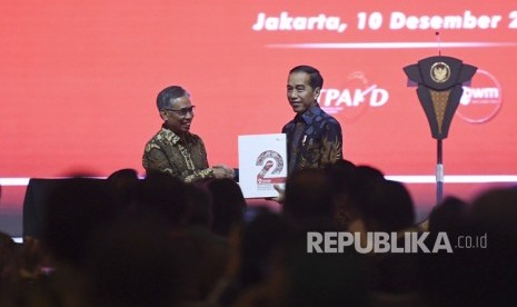 Ketua Dewan Komisioner Otoritas Jasa Keuangan (OJK) Wimboh Santoso (kiri) menyerahkan buku dua tahun Bank Wakaf Mikro (BWM) kepada Presiden Joko Widodo (kanan) saat Rapat Koordinasi Nasional Tim Percepatan Akses Keuangan Daerah (TPAKD) dan Silahturahmi Nasional Bank Wakaf Mikro 2019 di Jakarta, Selasa (10/12/2019).