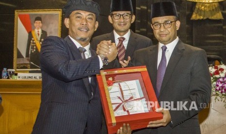 Ketua DPRD DKI Jakarta Prasetio Edi Marsudi (kiri) menyerahkan hasil rapat paripurna kepada Gubernur DKI Jakarta Anies Baswedan (kanan), disaksikan Wakil Gubernur DKI Jakarta Sandiaga Uno (tengah), saat rapat paripurna pengesahan Raperda menjadi Perda tentang Anggaran Pendapatan dan Belanja Daerah (APBD) DKI Tahun 2018, di DPRD DKI Jakarta, Jakarta, Selasa (30/11).