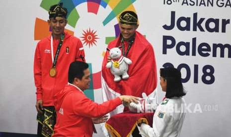 Ketua INASGOC Erick Tohir (kiri bawah) memberikan medali emas kepada pasangan pesilat Indonesia peraih medali emas Yola Primadona Jampil (kanan atas)-Hendy (kiri atas) saat upacara penyerahan medali nomor tunggal putri pencak silat seni Asian Games 2018 di Padepokan Pencak Silat Taman Mini Indonesia Indah (TMII), Jakarta, Senin (27/8).