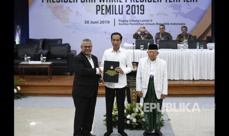 Ketua KPU Arief Budiman (kiri) menyerahkan surat keputusan KPU tentang Penetapan Hasil Pemilu 2019 kepada Presiden dan Wakil Presiden terpilih periode 2019-2024, Joko Widodo (tengah) dan KH Ma'ruf Amin (kanan) di gedung KPU, Jakarta, Ahad (30/6/2019). 