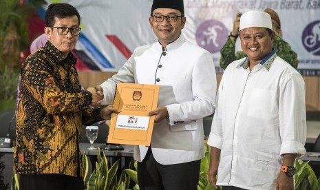 Ketua KPU Jabar Yayat Hidayat (kiri) memberikan berkas berita acara dan surat keputusan kepada pasangan Gubernur dan Wakil Gubernur Jawa Barat terpilih Ridwan Kamil (tengah) dan Uu Ruzhanul Ulum (kanan) saat rapat pleno terbuka Penetapan Pasangan Calon Terpilih pada Pilgub Jabar 2018 di Bandung, Jawa Barat, Selasa (24/7). 