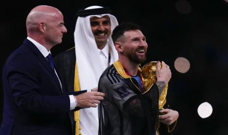 Lionel Messi dari Argentina mengangkat trofi yang diapit oleh Presiden FIFA Gianni Infantino dan Emir Qatar Sheikh Tamim bin Hamad Al Thani setelah memenangkan pertandingan sepak bola final Piala Dunia antara Argentina dan Prancis di Stadion Lusail di Lusail, Qatar, Ahad (18/12/2022). Haru dan Bangga, Cerita Pembuat Jubah Bisht yang Dikenakan Messi