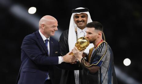  Lionel Messi (Kanan) dari Argentina mengenakan jubah tradisional Arab Bisht menerima trofi dari Presiden FIFA Gianni Infantino (Kiri) dan Sheikh Tamim bin Hamad Al Thani (Tengah), Emir Qatar, setelah memenangkan Final Piala Dunia FIFA 2022 antara Argentina dan Prancis di stadion Lusail di Lusail, Qatar,  Ahad, 18 Desember 2022.