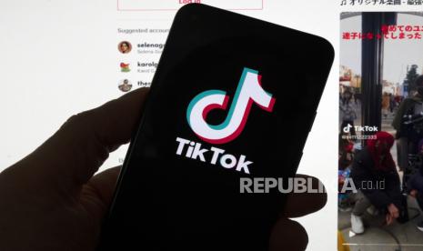 Logo TikTok ditampilkan pada telepon seluler di depan layar komputer yang menampilkan beranda TikTok.