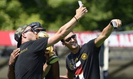 Lukas Podolski (kiri) dan Mesut Ozil (kanan) melakukan selfie dengan trofi Piala Dunia