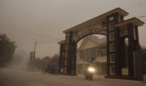   Pengguna jalan melintas di depan SMAN 1 Seyegan yang tertutup abu vulkanik di Margoagung, Seyegan, Sleman, Yogyakarta, Jumat (14/2). (Antara/Andreas Fitri Atmoko) 