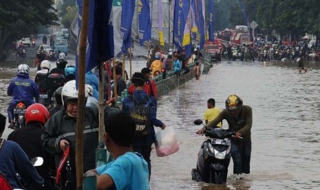 Warga berusaha menerobos genangan air di Jalan KH. Abdulah Syafei,Kampung Melayu Besar, Jakarta, Ahad (23/2). (Republika/Tahta Aidilla)