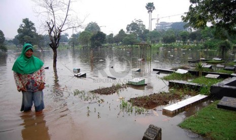   Seorang perawat makam melintasi air banjir yang melanda Tempat Pemakaman Umum (TPU) Karet Bivak, Tanah Abang, Jakarta Pusat, Kamis (27/2). (foto : Raisan Al Farisi)