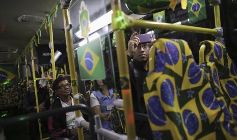   Seorang penumpang menggunakan ponsel mengabadikan bus kota yang dihiasi dengan warna bendera Brasil dan motif Piala Dunia 2014 di Santo Andre, pinggiran kota Sao Paulo, Rabu (18/6). (REUTERS/Nacho Doce)