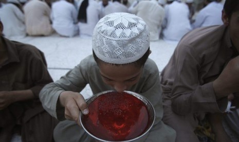 Seorang anak laki-laki minum air sirup saat berbuka puasa, pada hari pertama bulan Ramadhan di sebuah masjid di Peshawar, Pakistan (29/6).  (Reuters/Fayaz Aziz)