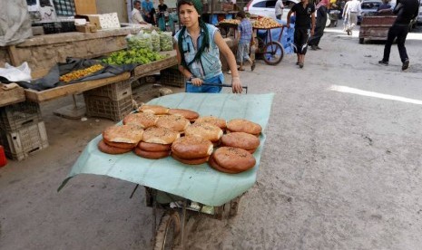   Seorang anak menjual roti manis di hari pertama bulan suci Ramadhan di lingkungan kota Aleppo, Suriah, Ahad (29/6). (Reuters/Hosam Katan)