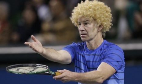 Mantan petenis nomor satu dunia asal AS John McEnroe, mengenakan wig saat bermain dalam pertandingan tenis amal melawan petenis Jepang Kei Nishikori di Tokyo, Ahad (17/11).  (AP/Shizuo Kambayashi)