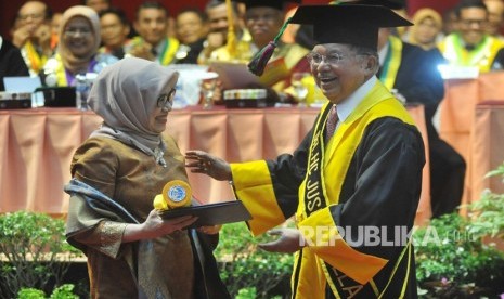 Mantan Wakil Presiden Jusuf Kalla (kanan) menyerahkan sertifikat kepada istrinya, Mufidah Jusuf Kalla (kiri), saat penganugerahan gelar doktor kehormatan (Dr. HC) di Universitas Negeri Padang (UNP) Padang, Sumatera Barat, Kamis (5/12/2019).