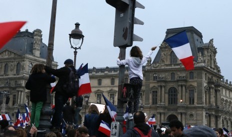 Masyarakat mengibarkan bendera Prancis di kawasan Museum Louvre tempat Emmanuel Macron disebut akan merayakan kemenangannya dalam pemilu Prancis, (8/5).