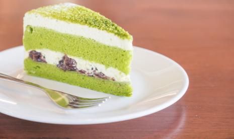 Matcha cake dengan olesan krim dan buah di bagian tengahnya.