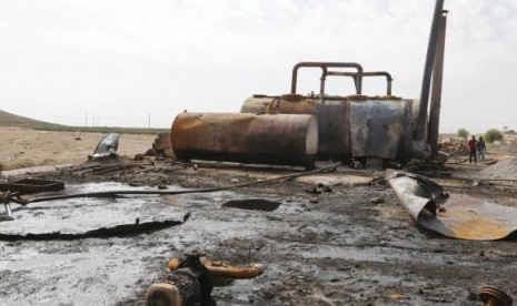 Men walk past damage at an oil refinery and a gas station that were targeted by what activists said were US-led air strikes, in Tel Abyad, near the border with Turkey October 2, 2014. 