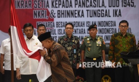 Menko Polhukam Wiranto (kiri) menyaksikan anak pemimpin Darul Islam/Tentara Islam Indonesia (DI/TII) Sekarmaji Marijan Kartosuwiryo, Sarjono Kartosuwiryo (kedua kiri) mencium bendera merah putih dalam acara pengucapan ikrar setia kepada Pancasila, UUD 45, NKRI dan Bhineka Tunggal Ika di Jakarta, Selasa (13/08/2019). 