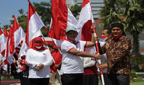 Menteri Dalam Negeri Tito Karnavian (tengah) didampingi Gubernur Jawa Timur Khofifah Indar Parawansa (kiri) menyerahkan Bendera Merah Putih kepada perwakilan warga saat acara Gerakan Nasonal Pembagian 10 Juta Bendera Merah Putih di Gedung Negara Grahadi, Surabaya, Jawa Timur, Ahad (14/8/2022). Kegiatan tersebut sebagai salah satu upaya dalam meningkatkan patriotisme dan nasionalisme masyarakat di seluruh Indonesia.