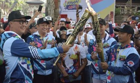 Menteri Sosial Agus Gumiwang Kartasasmita (kiri) menyulutkan api obor yang dibawa atlet Paralimpik cabang atletik I Nyoman Oka (kanan) disaksikan Ketua DPR RI Bambang Soesatyo (kedua kiri) saat Pawai Obor (Torch Relay) Asian Para Games 2018 di Denpasar, Bali, Minggu (16/9). 