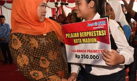 Menteri Sosial Khofifah Indar Parawansa (kiri) menyerahkan beasiswa kepada pelajar berprestasi saat penyaluran bantuan sosial nontunai Program Keluarga Harapan (PKH) di Alun-alun Kota Madiun, Jawa Timur, Senin (17/4). 