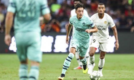 Mesut Oezil (tengah) menggiring bola saat membela Arsenal melawan PSG.