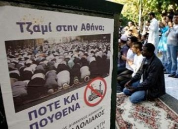 Muslim Yunani sholat di jalanan di dekat poster anti pembangunan masjid