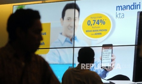 Nasabah melintasi banner iklan penawaran kredit tanpa agunan (KTA) yang ditawarkan di salah satu kantor cabang Bank Mandiri, Jakarta.