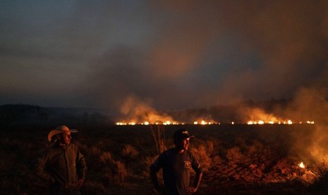 Neri dos Santos Silva (tengah) menyaksikan api yang mengancam peternakan tempatnya bekerja di kotamadya Nova Santa Helen, negara bagian Mato Grosso, Brasil, Jumat (23/8). Api itu bagian dari kebakaran yang terjadi di wilayah hutan Amazon.