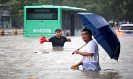  Orang-orang berjalan di jalan yang banjir setelah hujan deras yang melanda kota Zhengzhou di provinsi Henan, China tengah, Selasa, 20 Juli 2021. Perubahan iklim membuat bumi lebih sering dilanda cuaca ekstrem dan gelombang panas. 