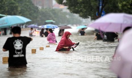  Orang-orang berjalan di jalan yang banjir setelah hujan deras yang melanda kota Zhengzhou di provinsi Henan, China tengah