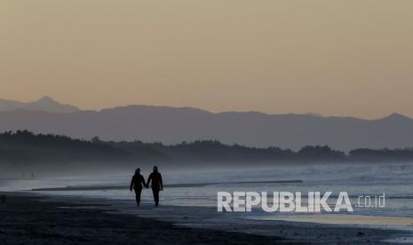 Orang-orang berjalan di sepanjang Pantai New Brighton saat matahari terbenam di Christchurch, Selandia Baru, Selasa (9/6). Warga Selandia Baru menikmati hari pertama mereka pada status level 1 setelah Perdana Menteri Jacinda Ardern mengumumkan pada Senin (8/6) bahwa Kabinet telah sepakat untuk mencabut hampir semua pembatasan akibat Covid-19.  