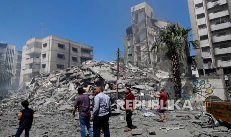 Orang-orang melihat puing-puing bangunan perumahan Yazegi yang dihancurkan oleh serangan udara Israel, di Kota Gaza, Ahad (16/5).