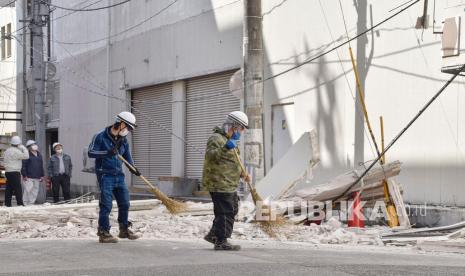  Orang-orang membersihkan jalan yang tertutup oleh tembok yang runtuh dari sebuah bangunan di Fukushima, Jepang utara Kamis, 17 Maret 2022. Gempa bumi kuat melanda di lepas pantai Fukushima di Jepang utara pada Rabu malam, menghancurkan perabotan, mematikan listrik dan membunuh beberapa orang. Tsunami kecil mencapai pantai, tetapi peringatan berisiko rendah dicabut pada Kamis pagi.